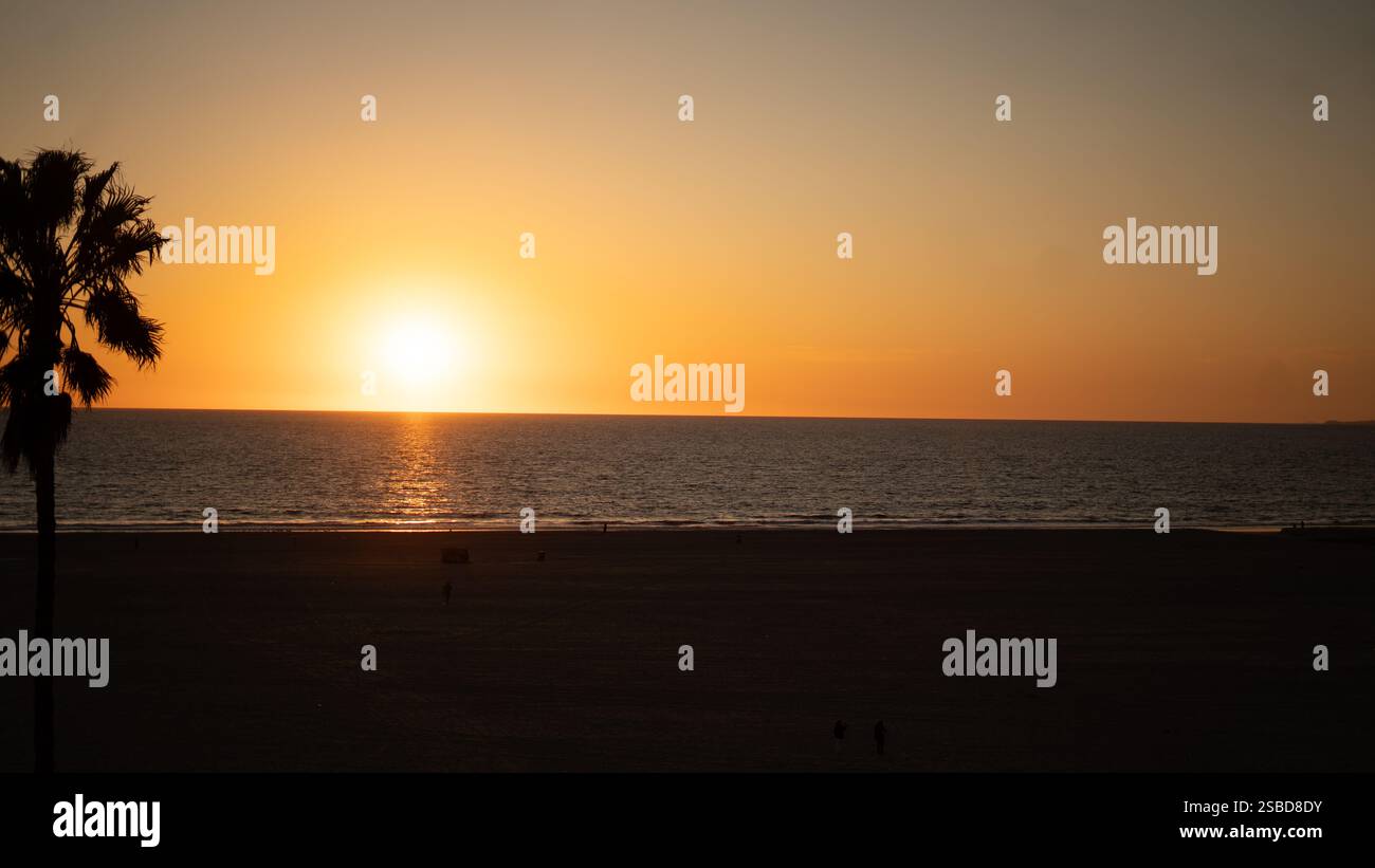 Uno splendido tramonto a Venice Beach, California, mentre il sole dorato affonda sotto l'orizzonte, dipingendo l'Oceano Pacifico con tonalità calde e vibranti. Foto Stock