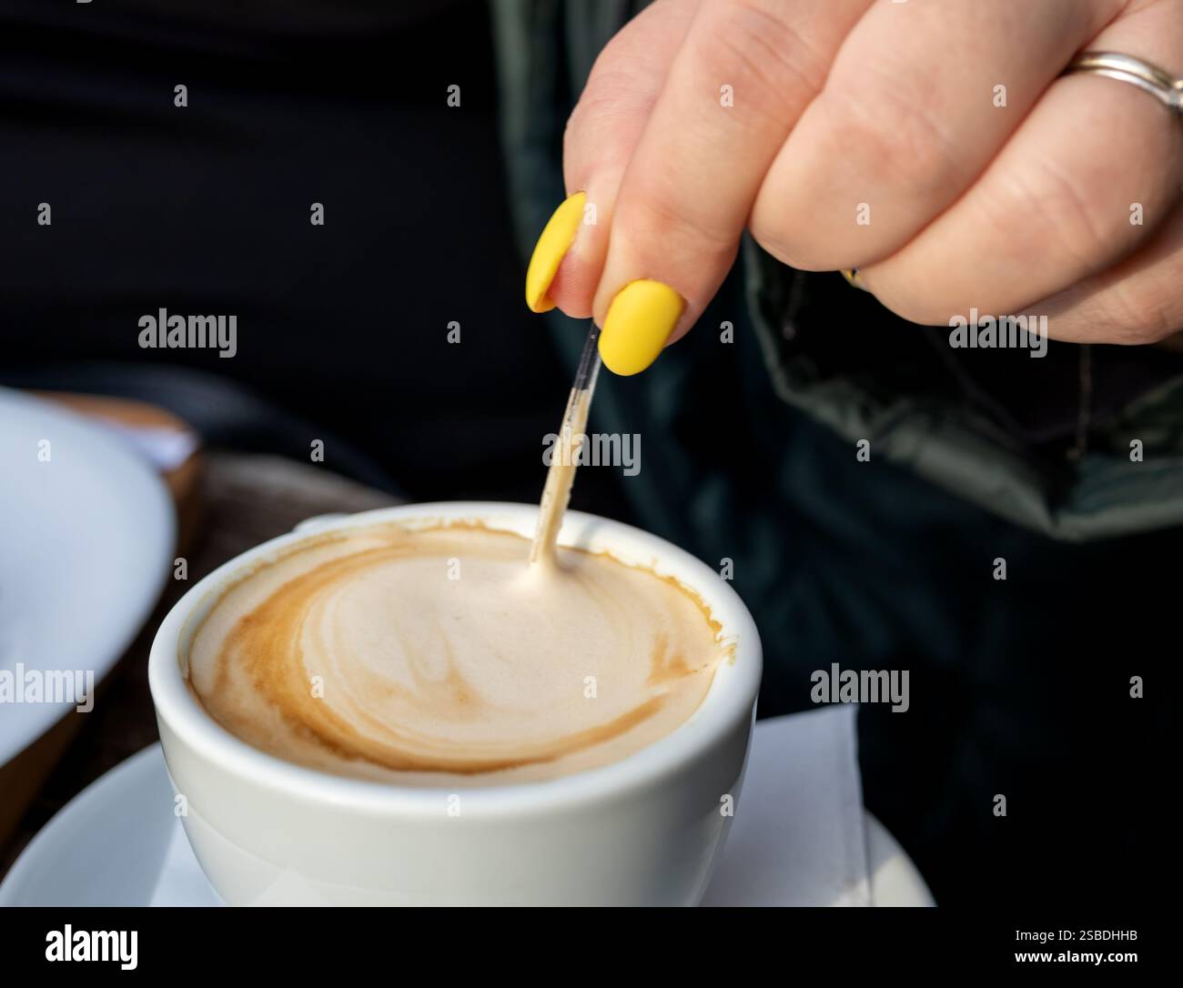 Una persona che mescola un cappuccino con un cucchiaio, primo piano sulla schiuma Foto Stock