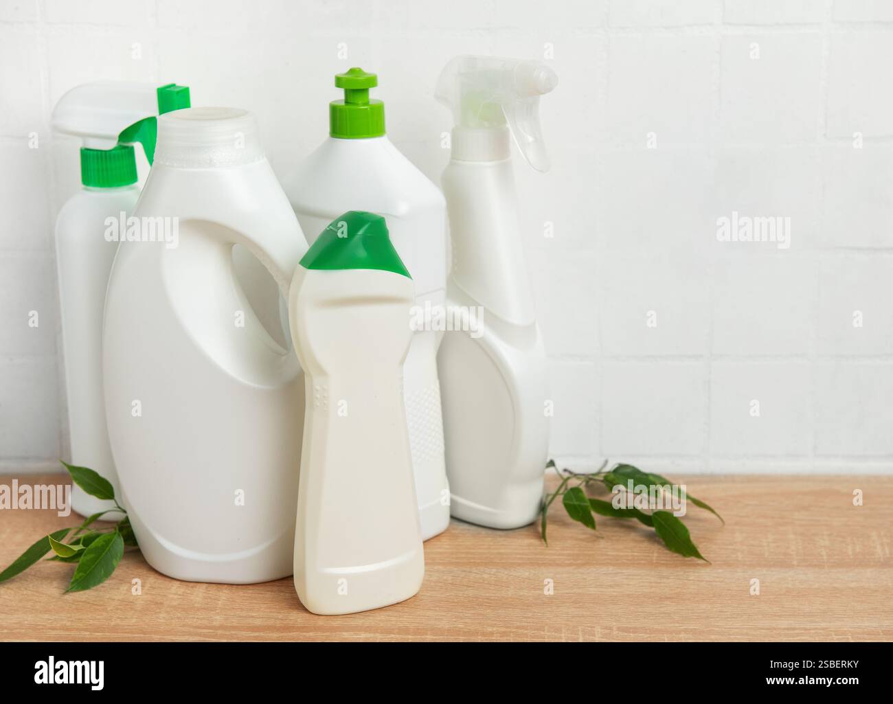 Bottiglie di plastica bianca con liquido detergente e foglie verdi sono posizionate su un ripiano in legno nel bagno Foto Stock