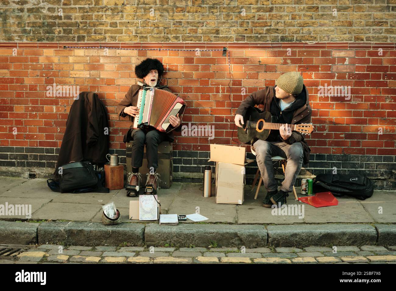 Due uomini che suonano una chitarra e una fisarmonica sul marciapiede (marciapiede) in Ezra Street vicino al mercato dei fiori di Columbia Road che si vendono per soldi. Foto Stock