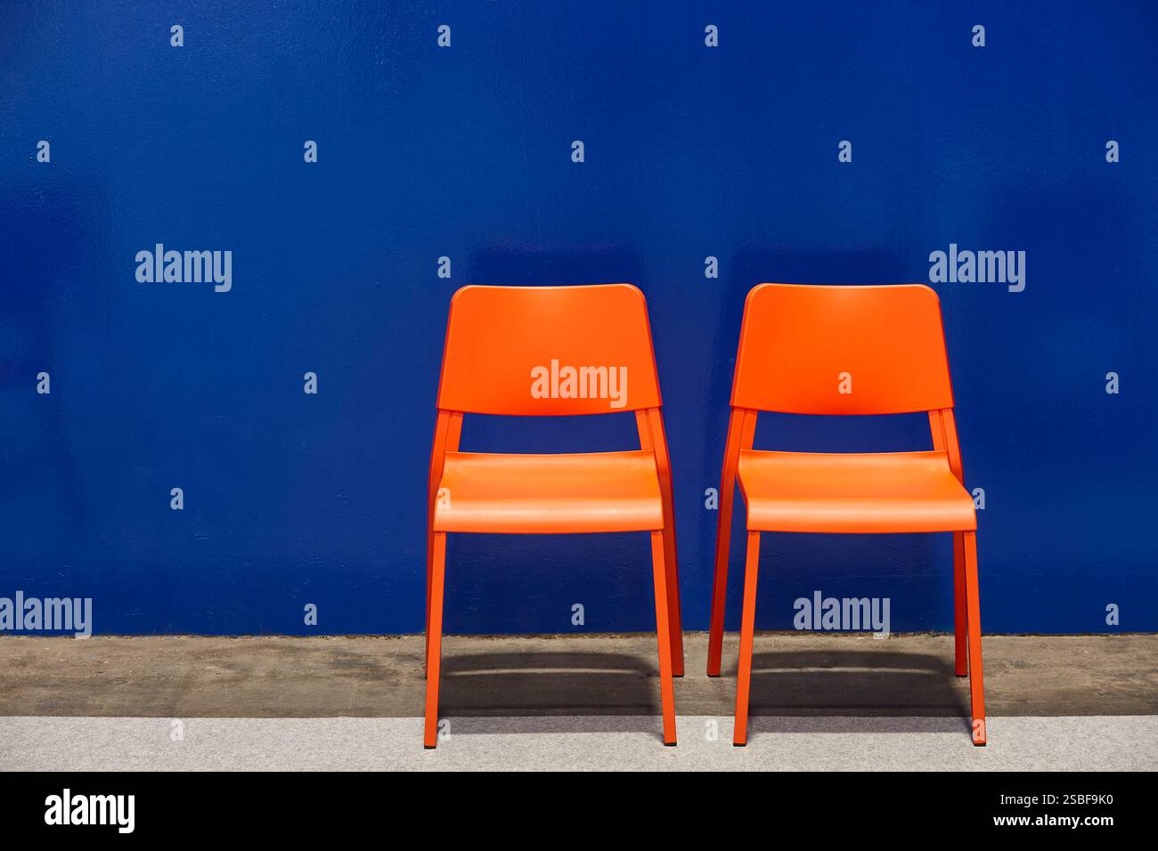 Due sedie di plastica di fronte a una parete blu. Minimalista Foto Stock