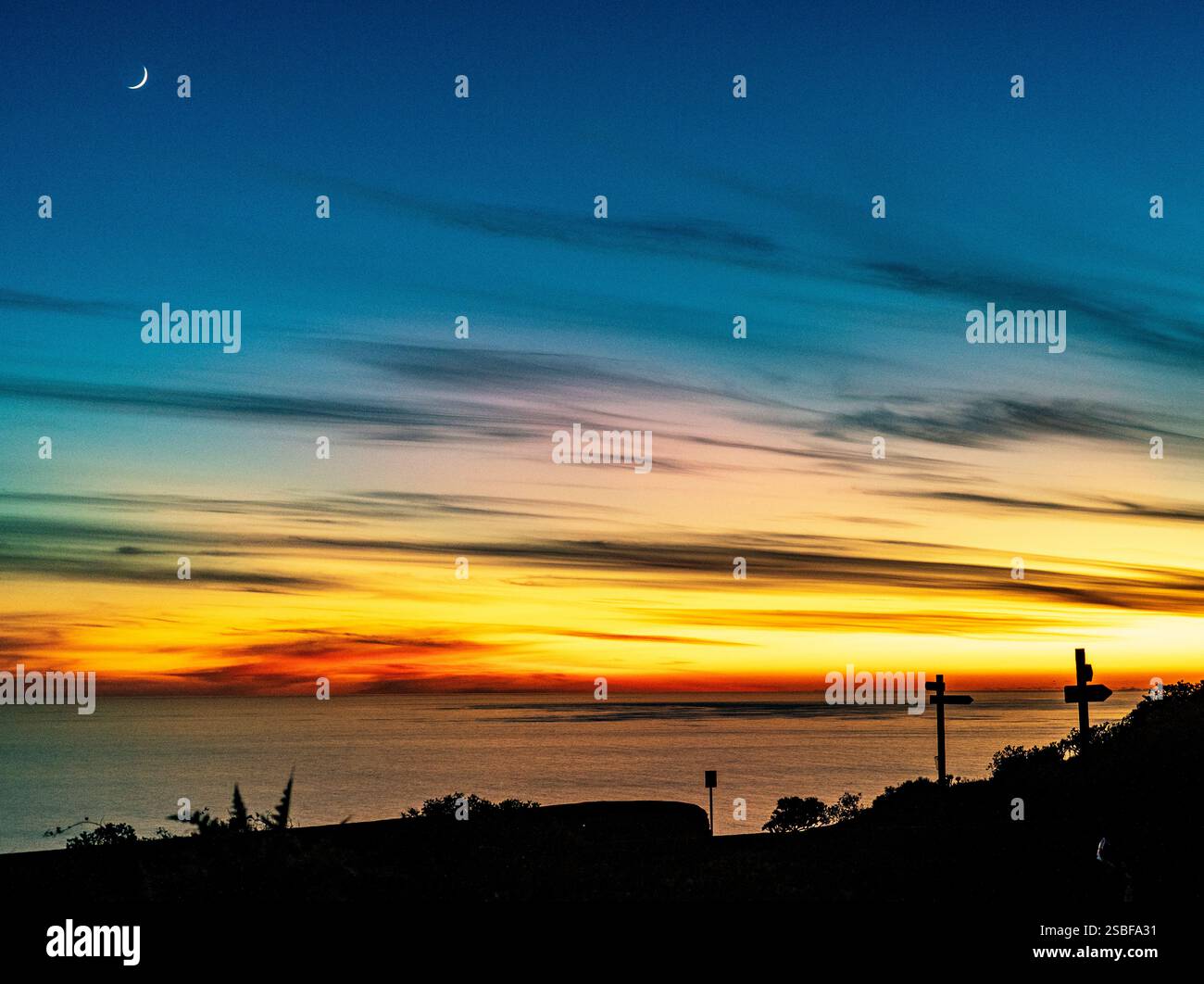 Un tranquillo tramonto sull'oceano, con vivaci sfumature di arancione e blu nel cielo. Le sagome di due croci sono visibili in primo piano e una mezzaluna Foto Stock