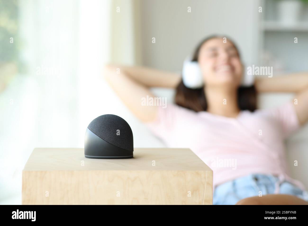 Donna felice che si rilassa ascoltando la musica da un altoparlante intelligente seduto sul divano di casa Foto Stock
