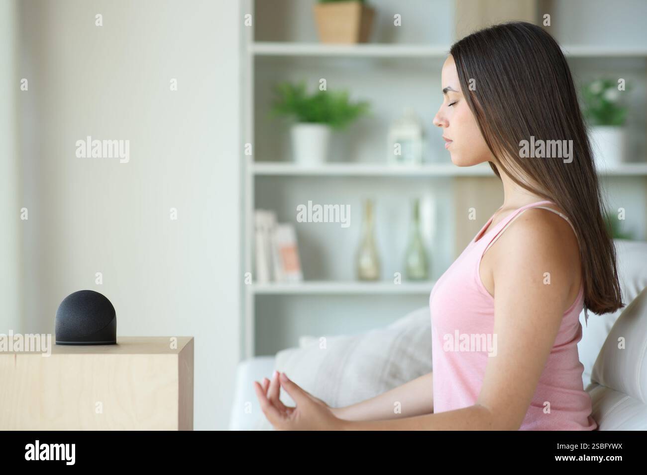 Donna che fa yoga con altoparlante intelligente seduto sul divano di casa Foto Stock