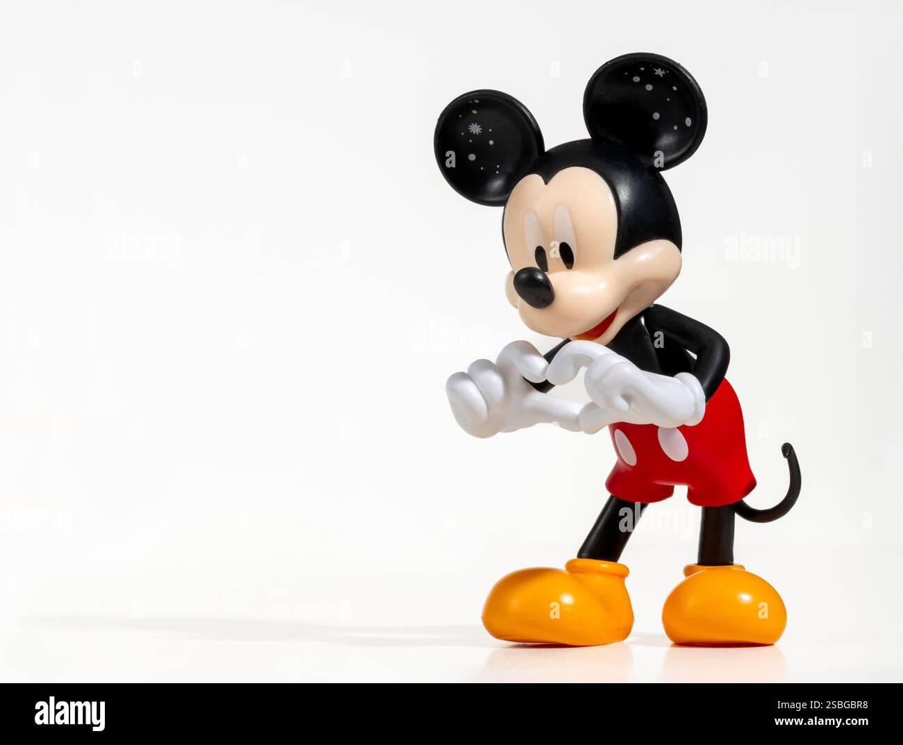 Statuetta in plastica di Topolino a forma di cuore con mani su sfondo bianco, concetto d'amore Foto Stock