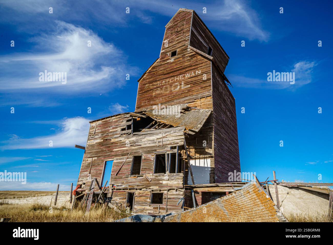 Un grande e vecchio edificio con una porta blu. L'edificio è in un campo. Il cielo è blu e ci sono nuvole Foto Stock