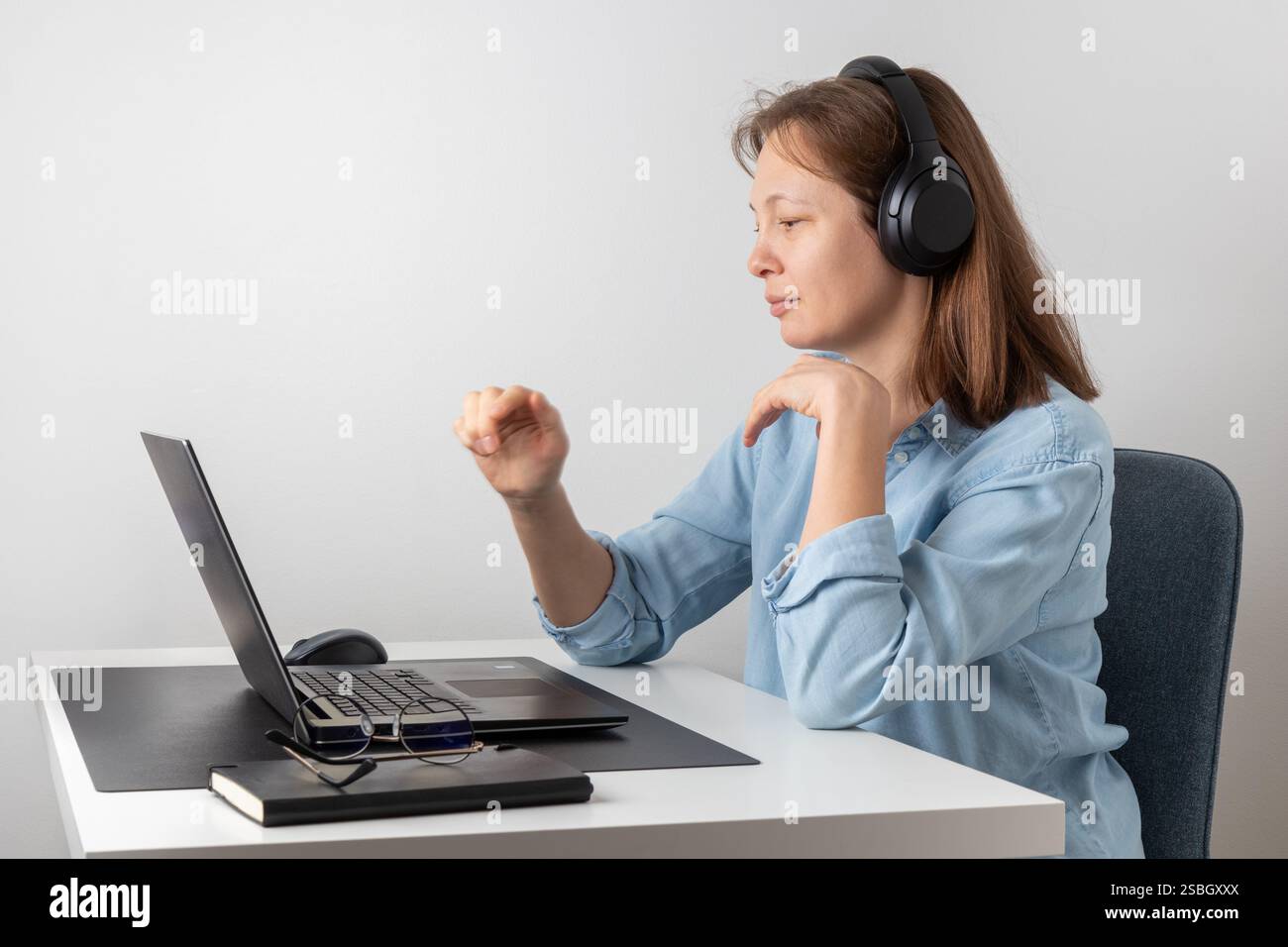 Una donna calma e sorridente con le cuffie che utilizzano il laptop, che guarda lo schermo del PC, lavora da casa come freelance. Postura corretta, ambiente buono Foto Stock