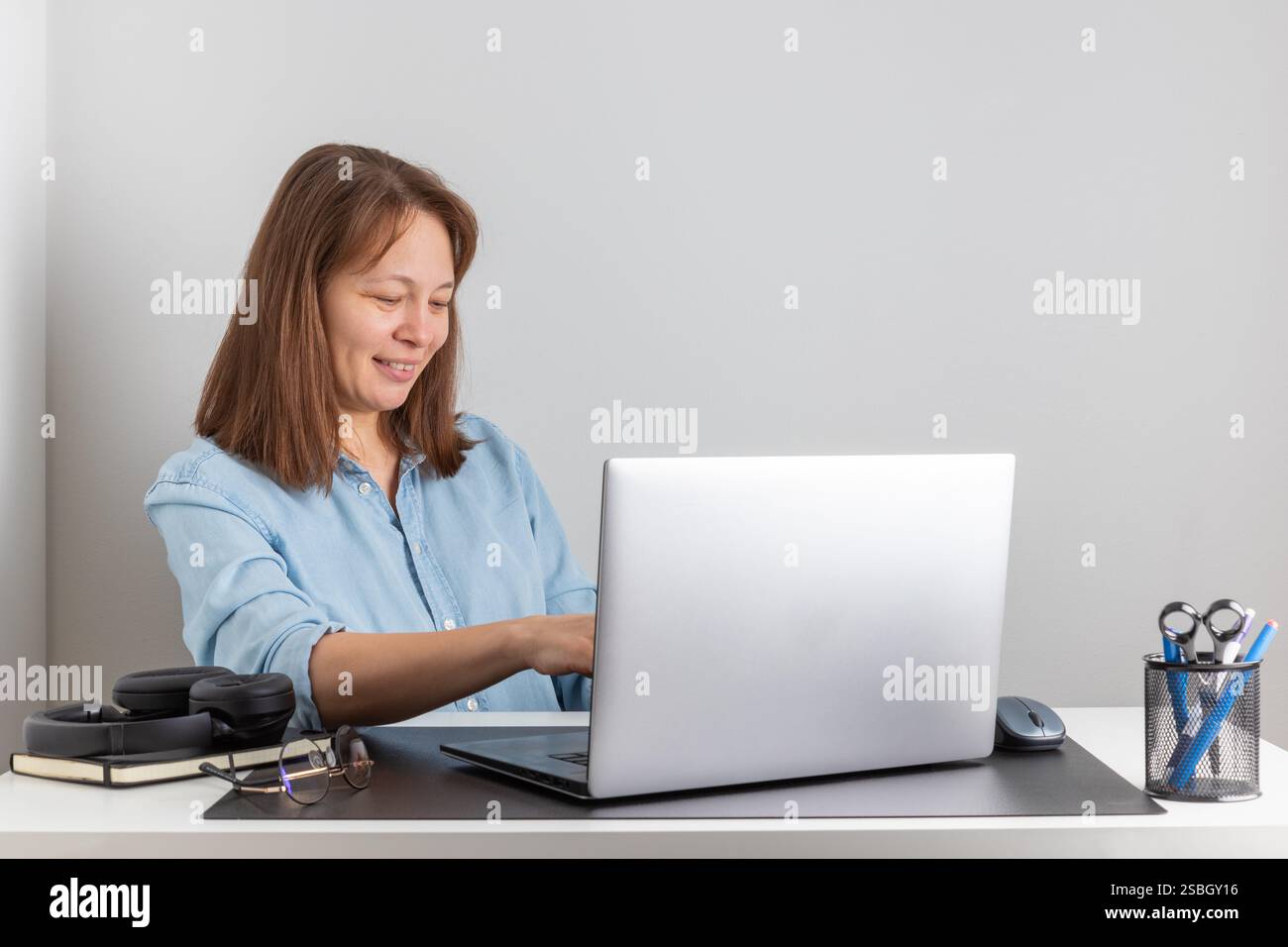 Una donna sorridente che digita sulla tastiera utilizzando un notebook, guarda lo schermo del PC, lavora da casa come libero professionista. Postura corretta Foto Stock