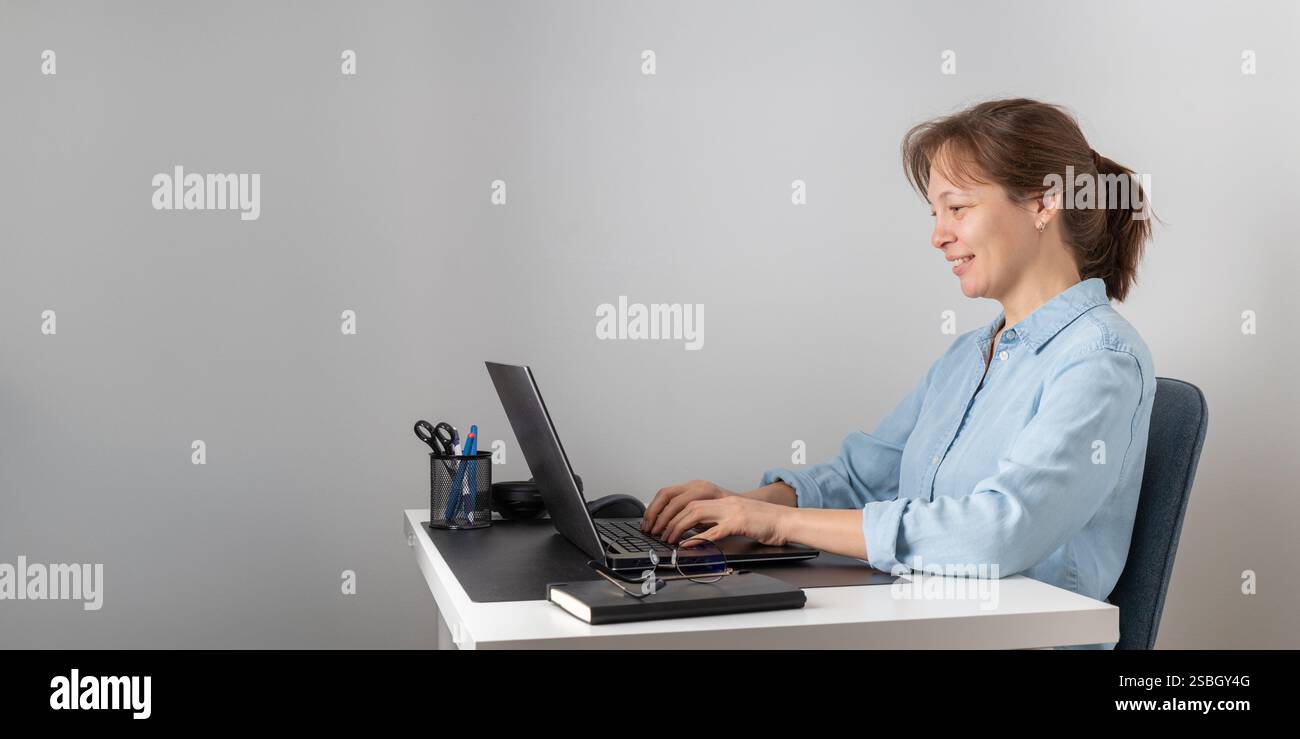 Una donna sorridente che digita sulla tastiera utilizzando un notebook, guarda lo schermo del PC, lavora da casa come libero professionista. Postura corretta Foto Stock