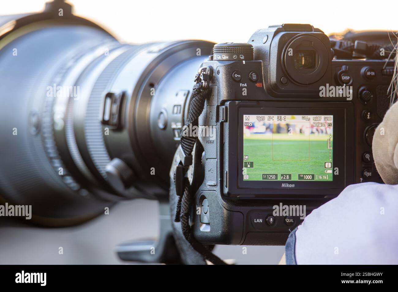 Primo piano di una fotocamera Nikon con teleobiettivo grande. È possibile visualizzare le impostazioni della fotocamera (iso, apertura, tempo di esposizione) Foto Stock