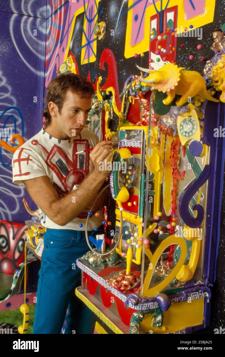 Kenny Scharf con il suo lavoro, 1985. Sharf è un pittore americano noto per la sua partecipazione alla scena artistica interdisciplinare dell'East Village di New York durante gli anni '1980, insieme a Jean-Michel Basquiat e Keith Haring. Fotografia di Bernard Gotfryd. Foto Stock