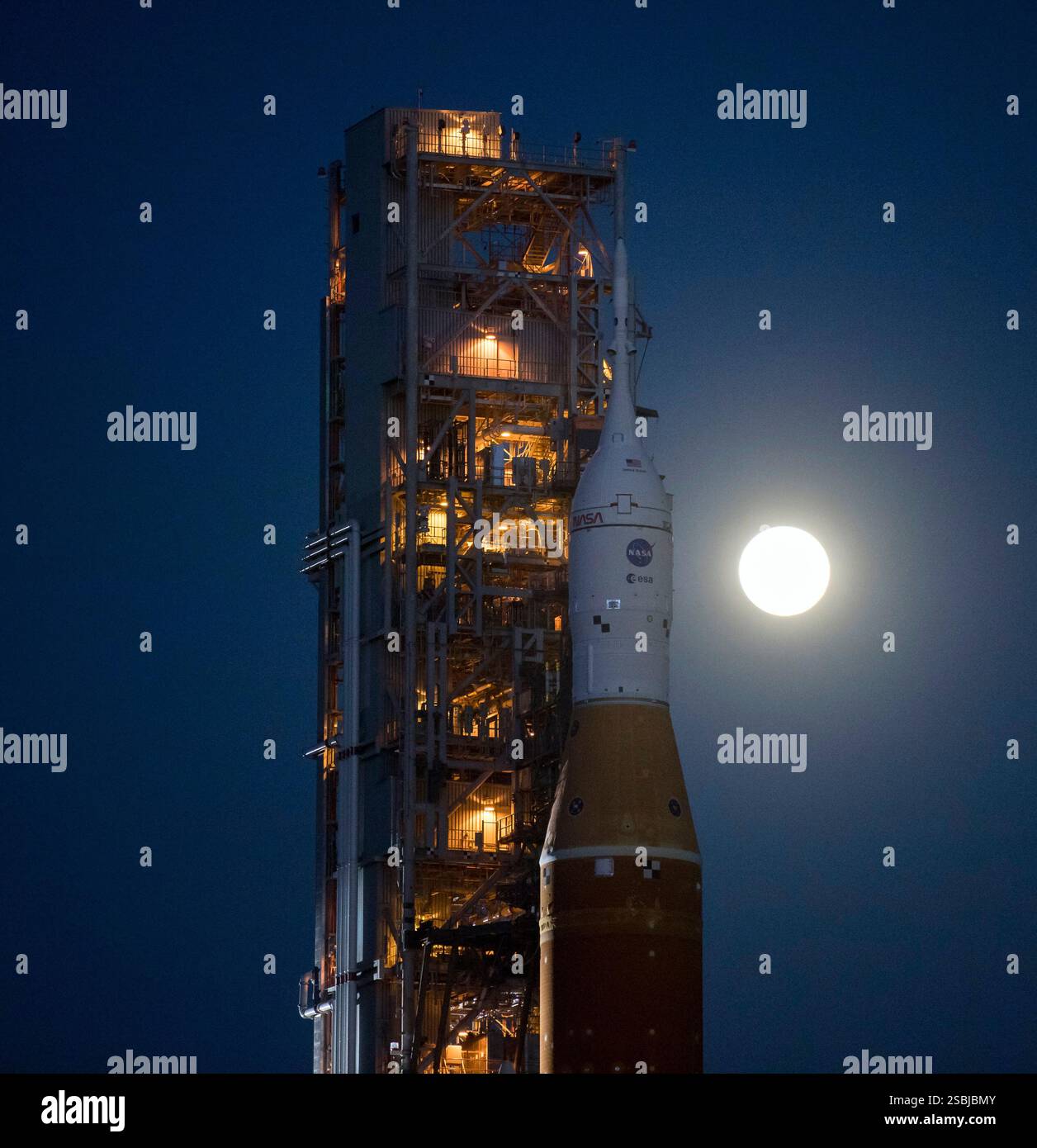 La Luna si vede sorgere dietro il razzo Space Launch System (SLS) della NASA con la navicella Orion a bordo in cima ad un lanciatore mobile mentre si lancia al Launch Complex 39B per la prima volta il 17 marzo 2022 al Kennedy Space Center della NASA in Florida. Prima del test di volo Artemis i della NASA, il razzo SLS completamente impilato e integrato e la navicella Orion saranno sottoposti a una prova di volo bagnata al Launch Complex 39B per verificare i sistemi e praticare le procedure di conto alla rovescia per il suo primo lancio. Foto Stock