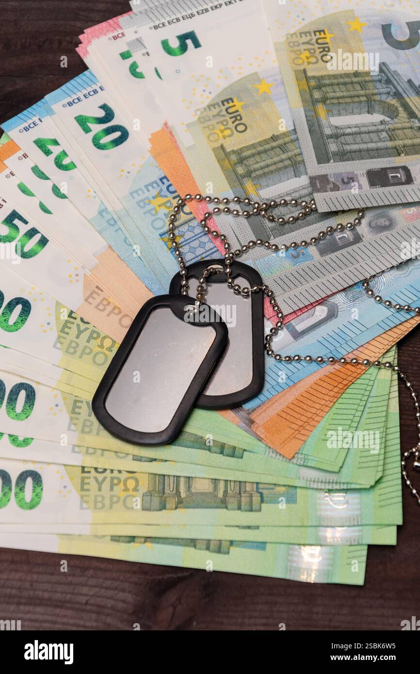 Il mucchio di denaro e il gettone militare simboleggiano i pagamenti ai soldati e le spese militari preventivate Foto Stock