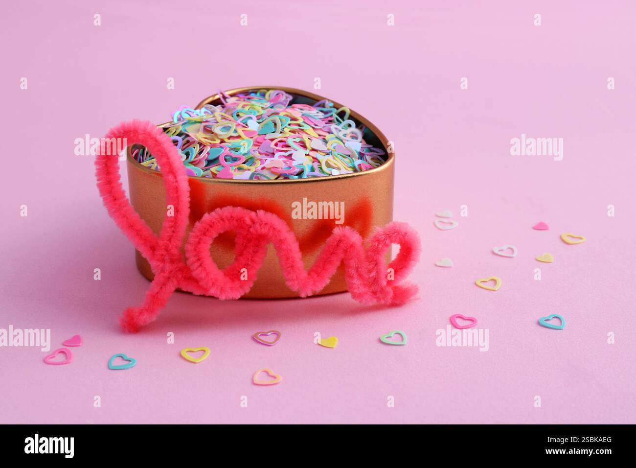 Parola d'amore accanto a un contenitore dorato pieno di cuori colorati Foto Stock