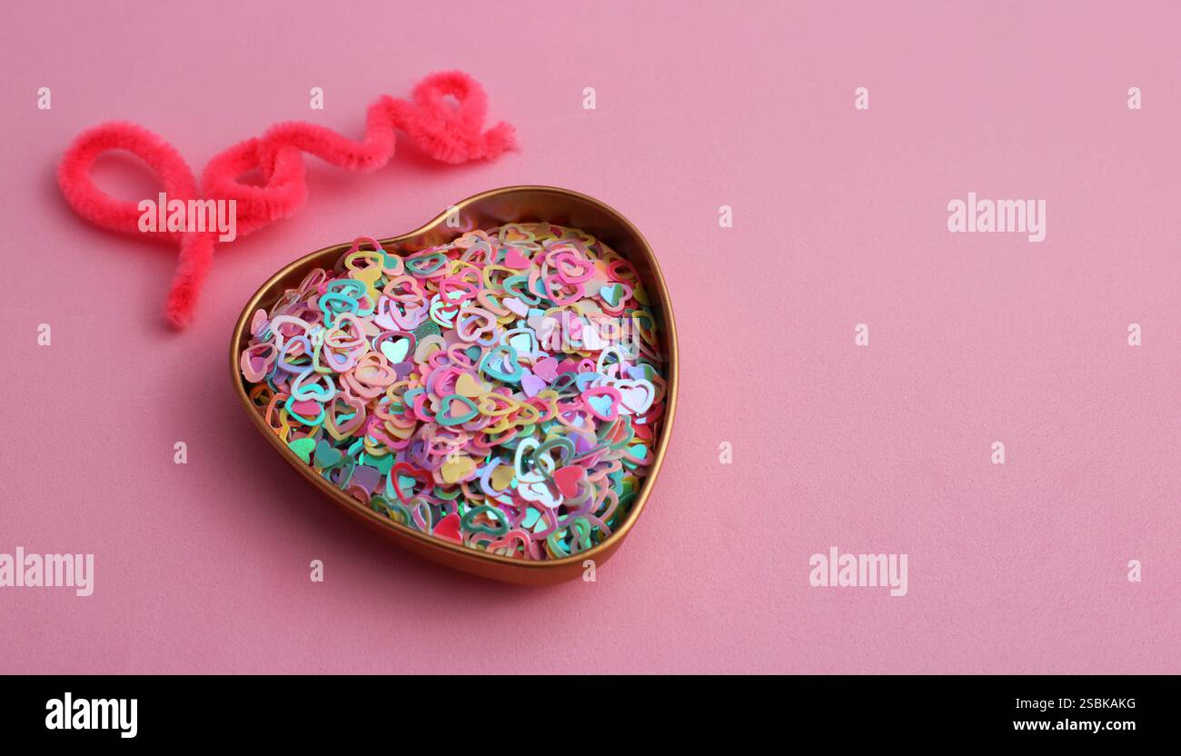 Parola d'amore accanto a un contenitore pieno di cuori colorati Foto Stock