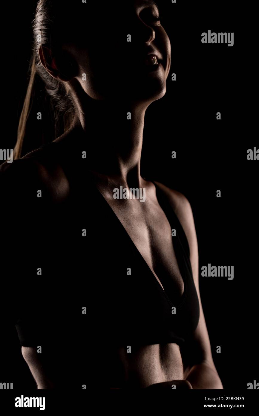 Silhouette di una donna in forma che indossa un reggiseno sportivo, che mostra una vita sana e una forma fisica in un ambiente minimalista e stimolante. Foto Stock