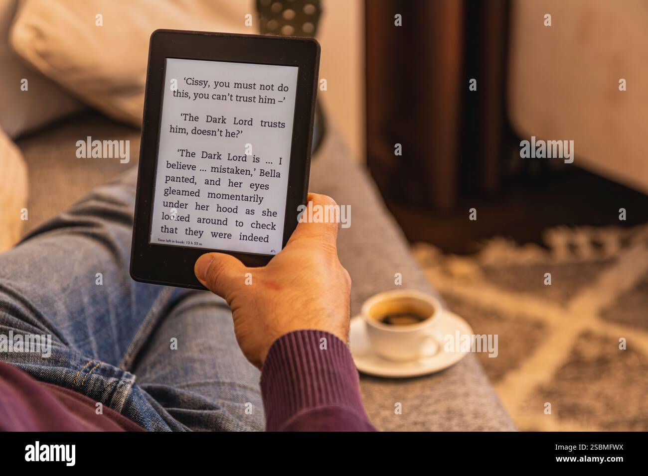 Rilassandosi a casa, una persona è immersa in un e-book, vivendo un'incantevole narrazione mentre si gusta una bevanda calda accanto a loro. L'atmosfera intima Foto Stock