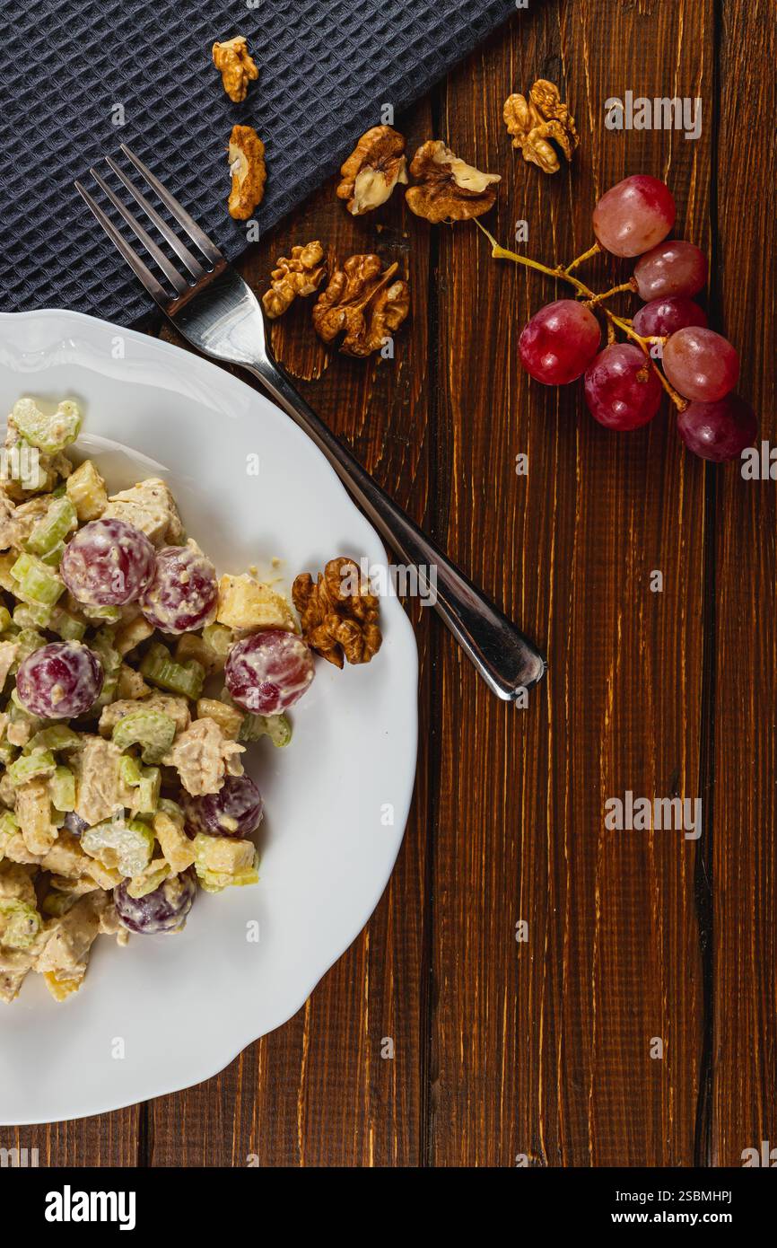 Una deliziosa insalata di pollo su un piatto bianco, abbinata a uva fresca e noci, si siede su un rustico tavolo di legno, creando un ambiente caldo per un sano sano Foto Stock