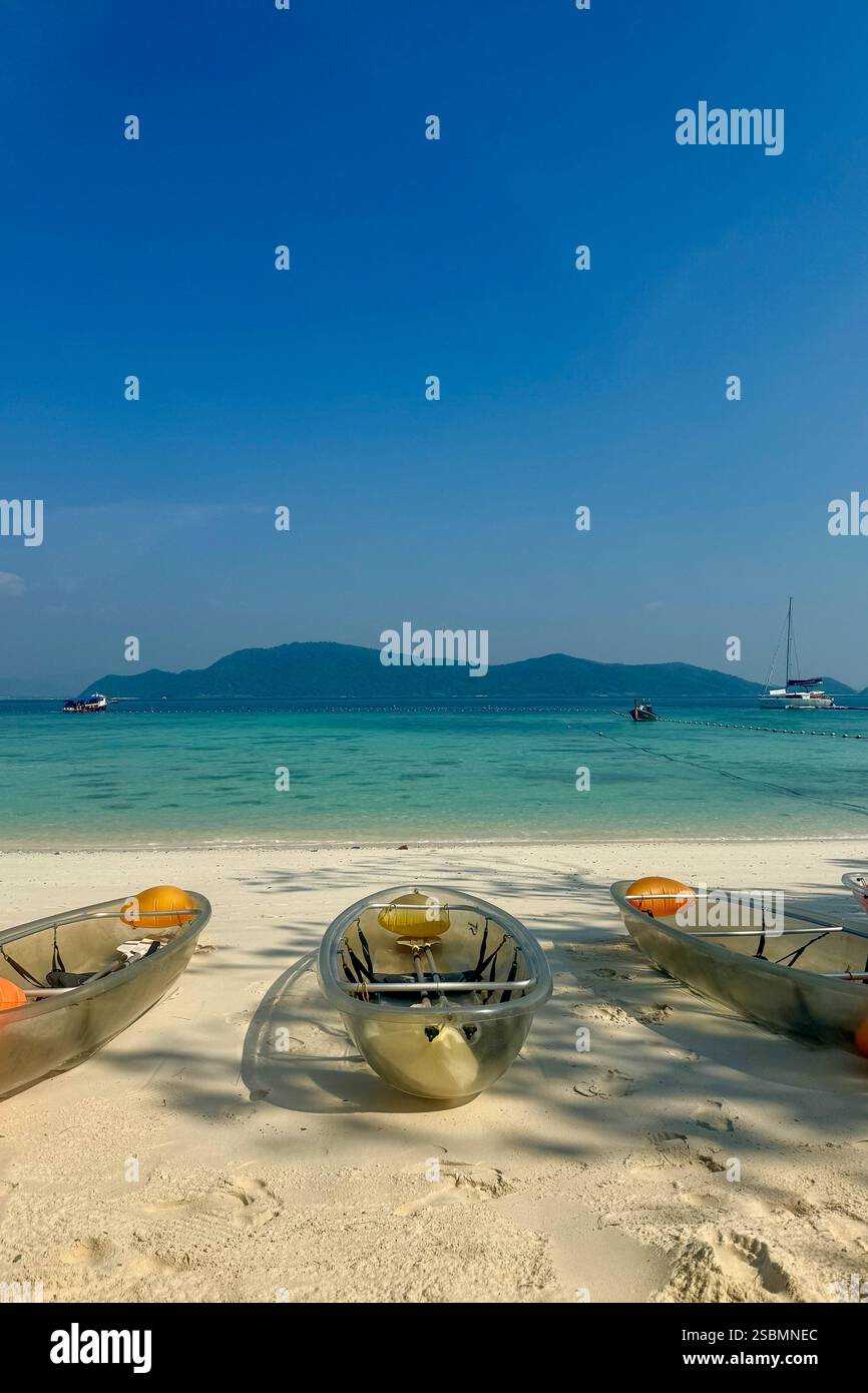 Kayak trasparenti su una spiaggia tropicale con acque turchesi Una tranquilla spiaggia tropicale con tre kayak trasparenti su soffice sabbia bianca, sopra Foto Stock