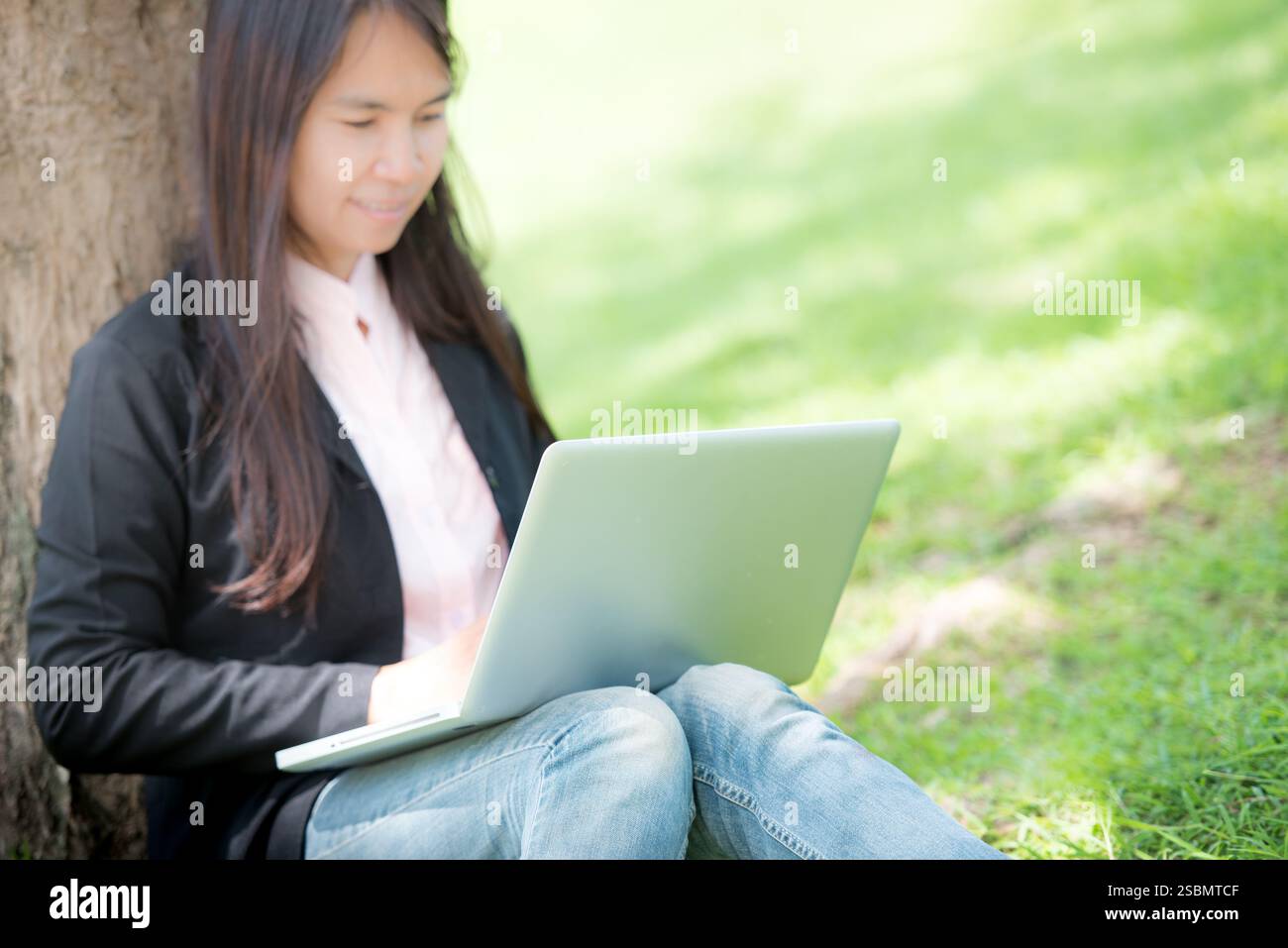 Donna asiatica seduta parco verde con computer portatile. Donna che lavora in un'azienda felice di un notebook che utilizza un notebook con le mani che digitano sulla tastiera Foto Stock