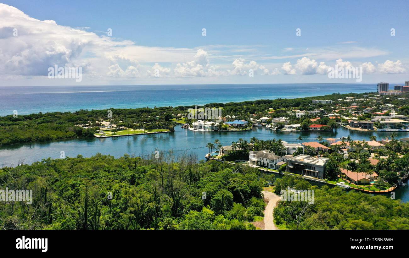 Uno splendido paesaggio costiero con residenze di lusso e vegetazione lussureggiante lungo un tranquillo corso d'acqua. Il cielo luminoso esalta i colori vivaci dello scenario Foto Stock