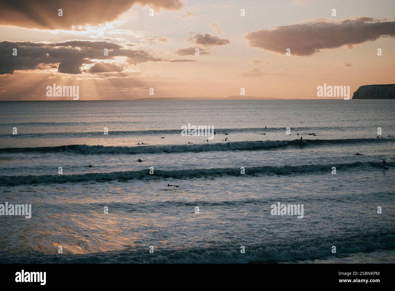 L'oceano è calmo e il cielo è di un bellissimo colore arancione. Il sole splende attraverso le nuvole, creando un'atmosfera calda e tranquilla Foto Stock