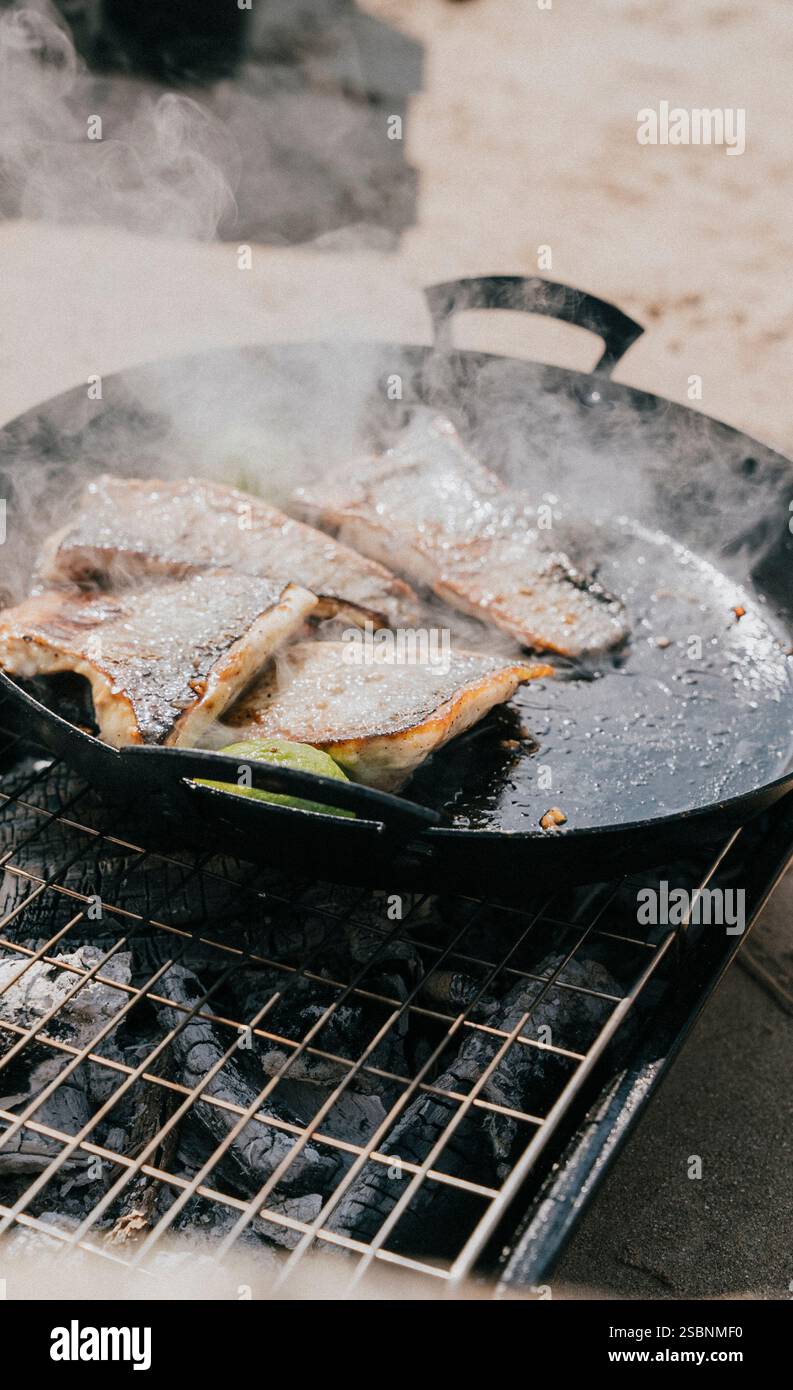 Una padella di pesce sta cucinando su una griglia. Il pesce è marrone e ha una consistenza croccante. La griglia è calda e il pesce è frizzante Foto Stock