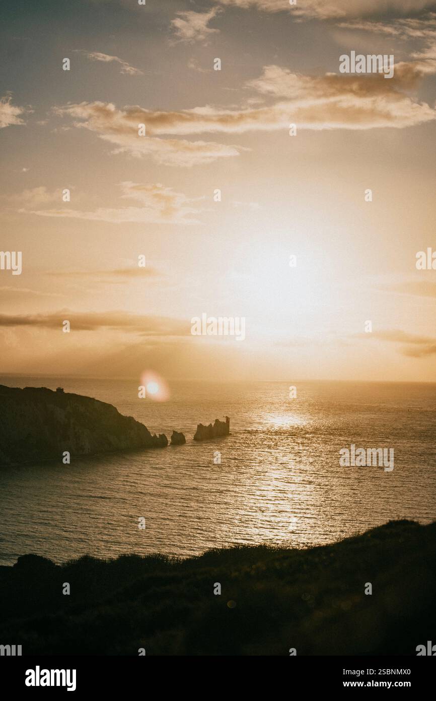 Il sole tramonta sull'oceano, proiettando un caldo bagliore sull'acqua. Il cielo è pieno di nuvole, creando un'atmosfera serena e tranquilla Foto Stock