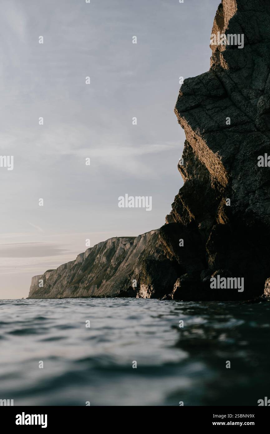 Una scogliera rocciosa si affaccia sull'oceano. Il cielo è nuvoloso e l'acqua è calma. La scena è serena e tranquilla Foto Stock