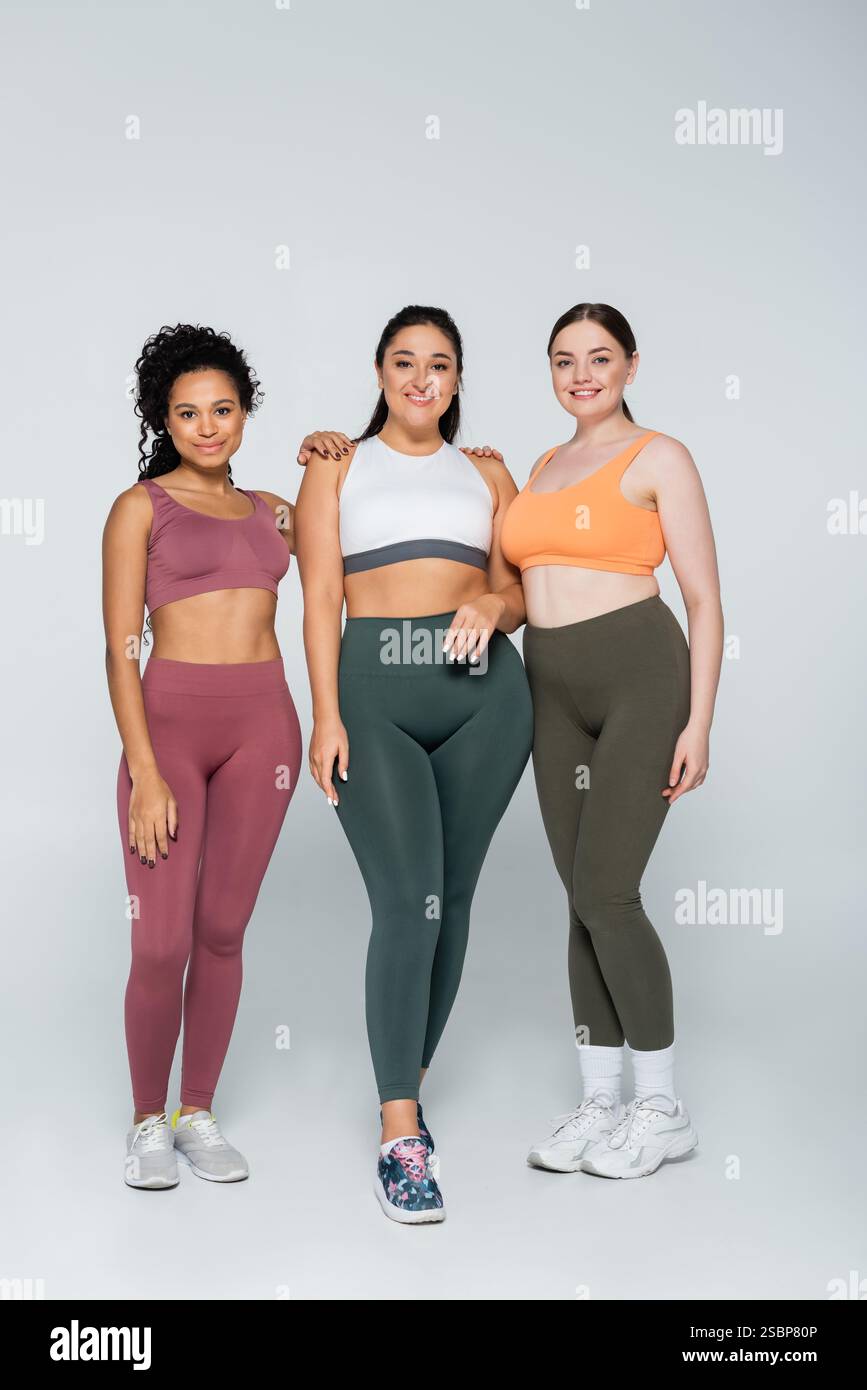 Tre donne sicure di sé si uniscono in un elegante abbigliamento fitness che celebra forza e bellezza. Foto Stock