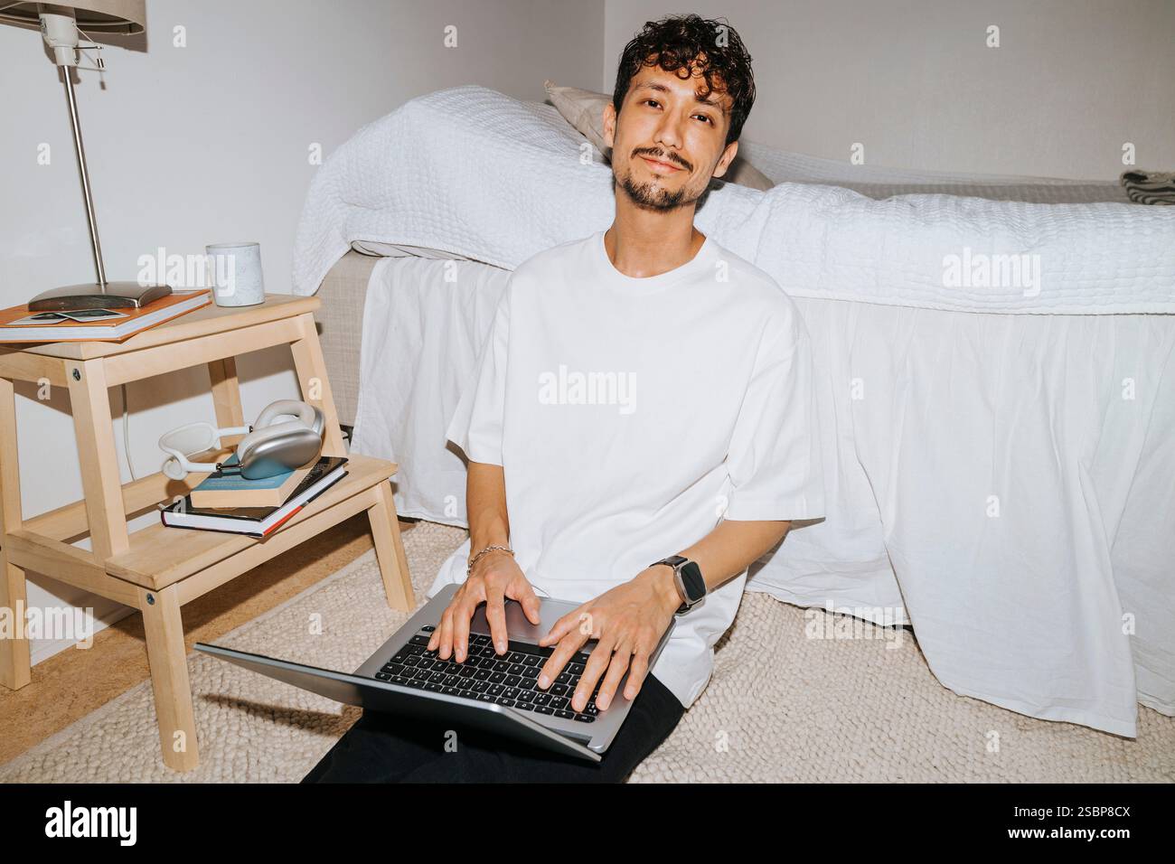 Ritratto di un giovane sorridente seduto con un laptop a letto nel dormitorio del college Foto Stock
