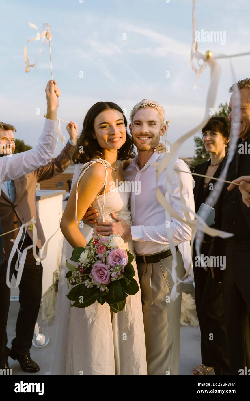 Ritratto della sposa e dello sposo felici in piedi con le braccia l'uno intorno all'altro durante la festa sul tetto Foto Stock