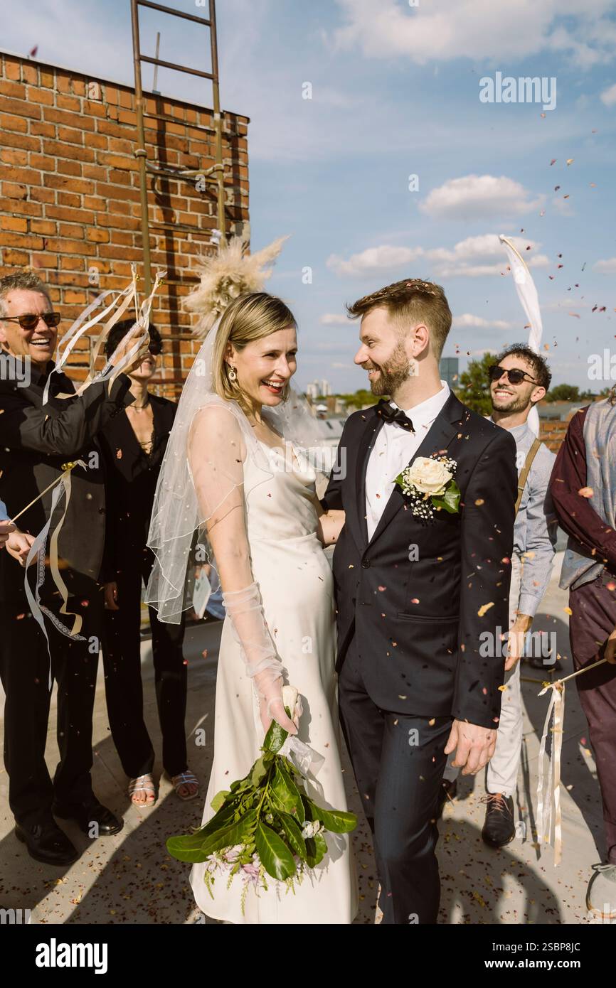 Ospiti felici che festeggiano la coppia appena sposata durante la celebrazione del matrimonio sul tetto Foto Stock
