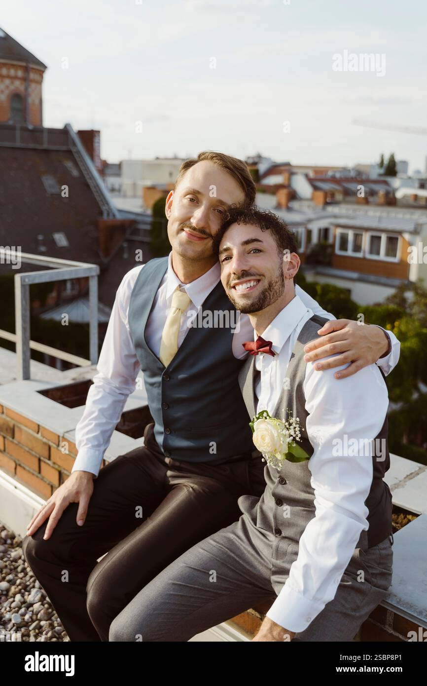 Ritratto di una coppia gay sposata sorridente seduta insieme sul tetto Foto Stock