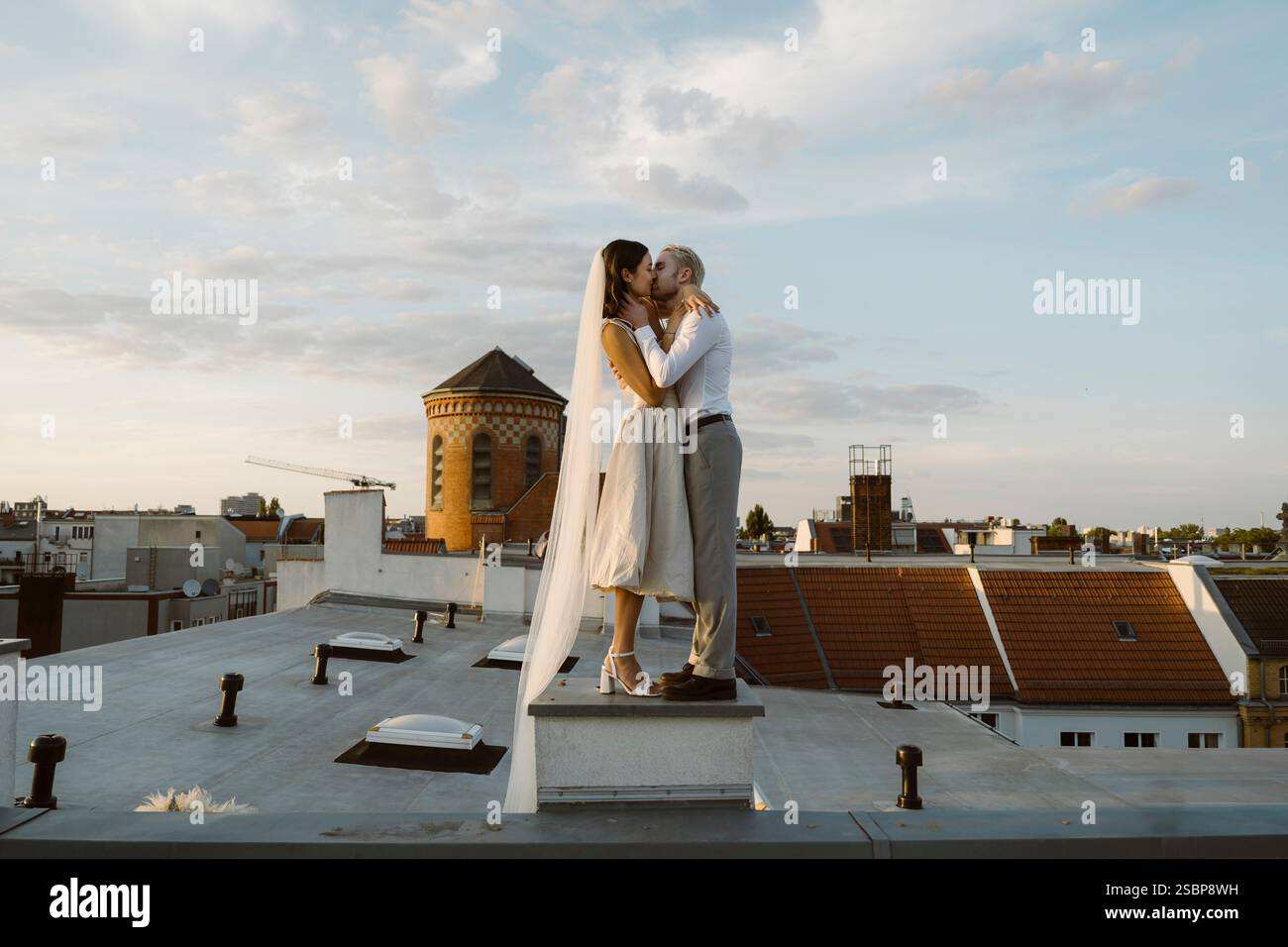 Giovane che bacia la sposa con un abito da sposa mentre si trova sul tetto Foto Stock