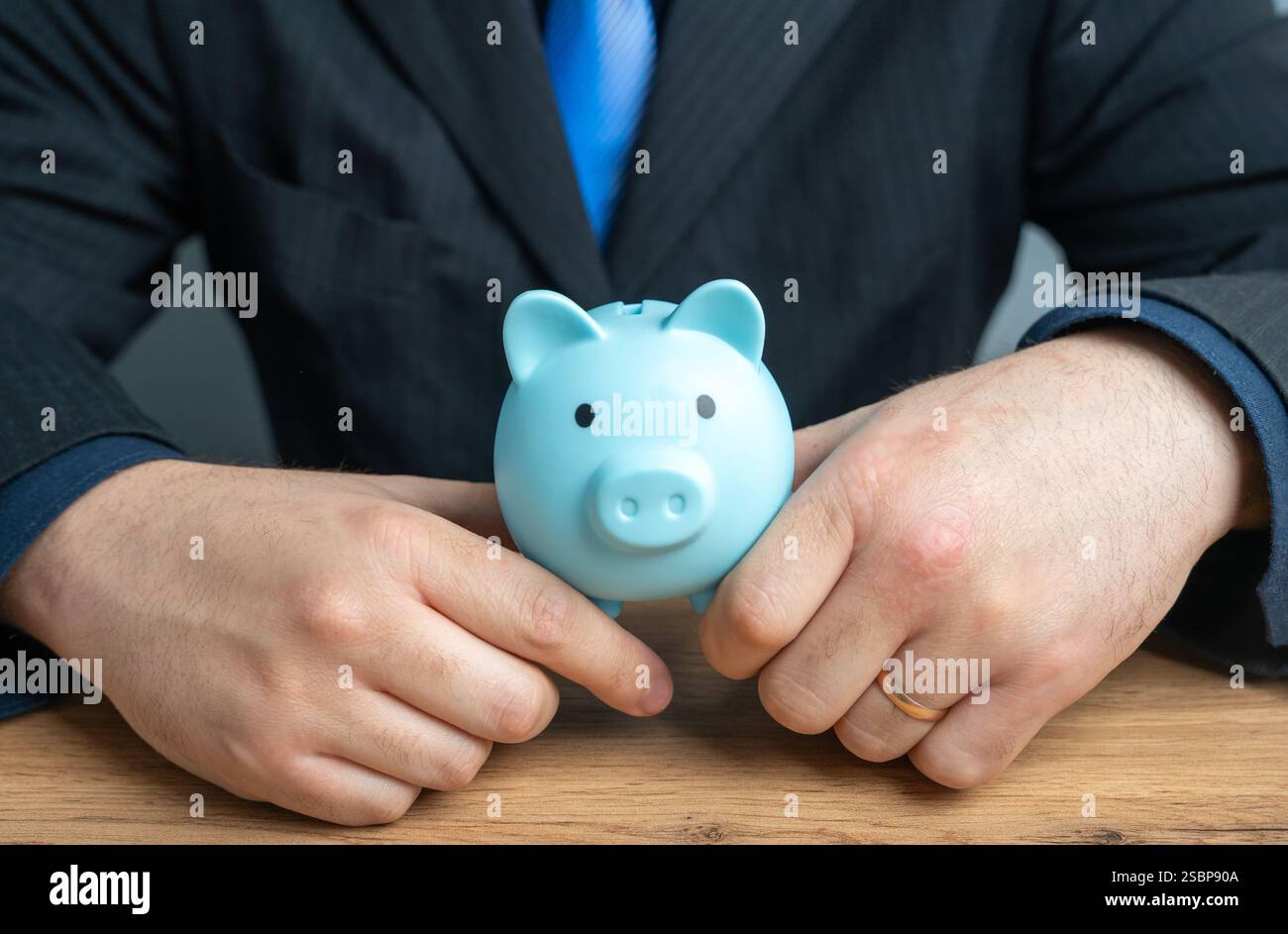 Un uomo d'affari ha in mano un salvadanaio. Il concetto di spavalderia e di politica finanziaria. Risparmi e capitali. Prestiti e depositi. Foto Stock