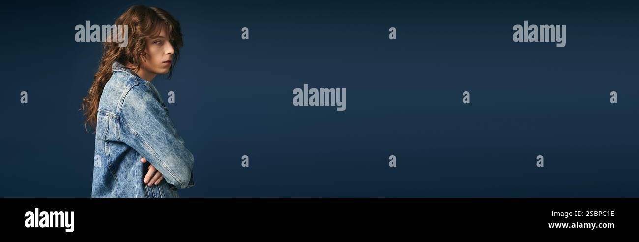 Un bel giovane uomo indossa con sicurezza un abbigliamento denim di tendenza, che mette in mostra il suo stile unico. Foto Stock