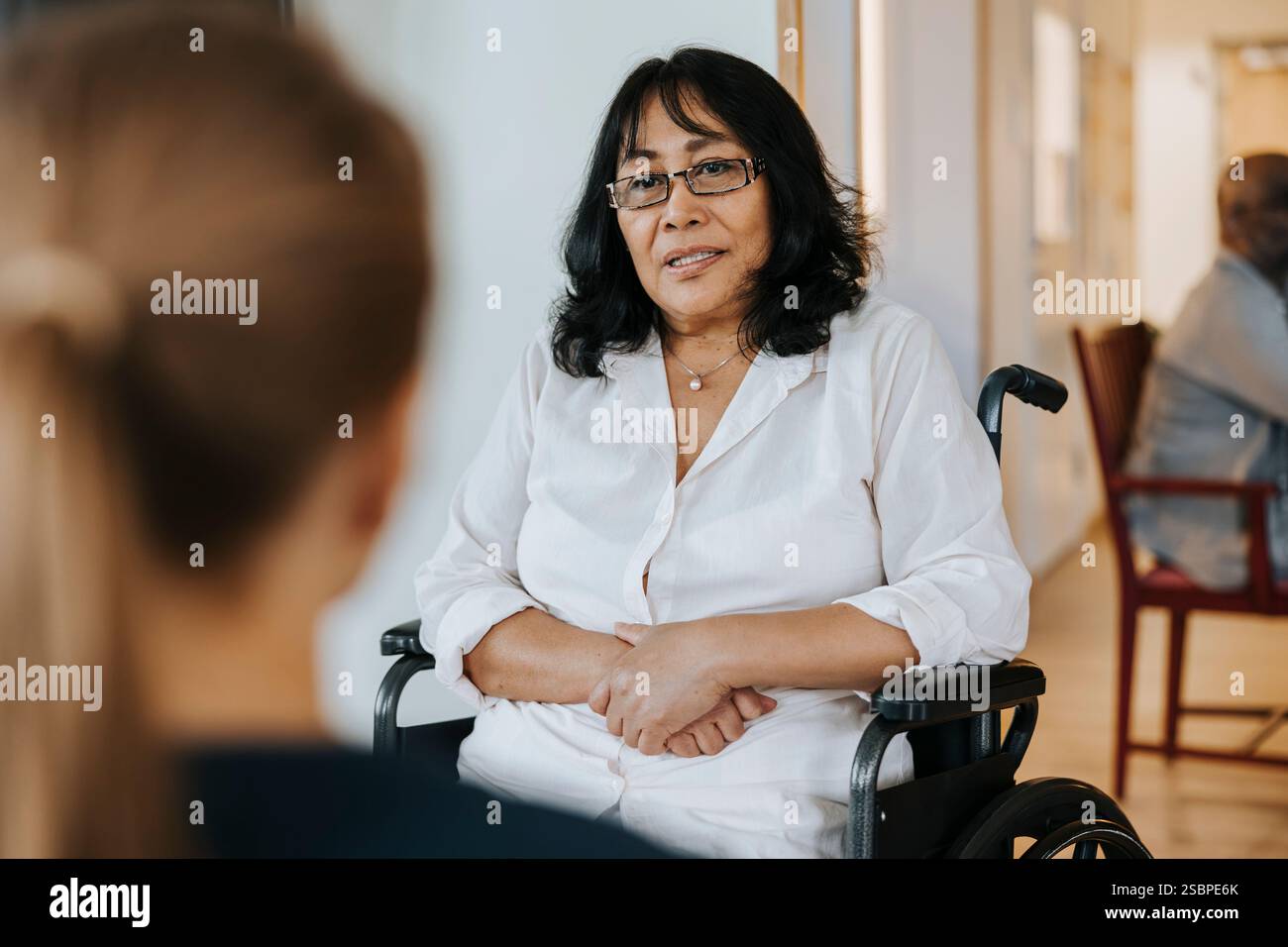 Donna anziana seduta in sedia a rotelle e che parla con una infermiera a casa di cura Foto Stock