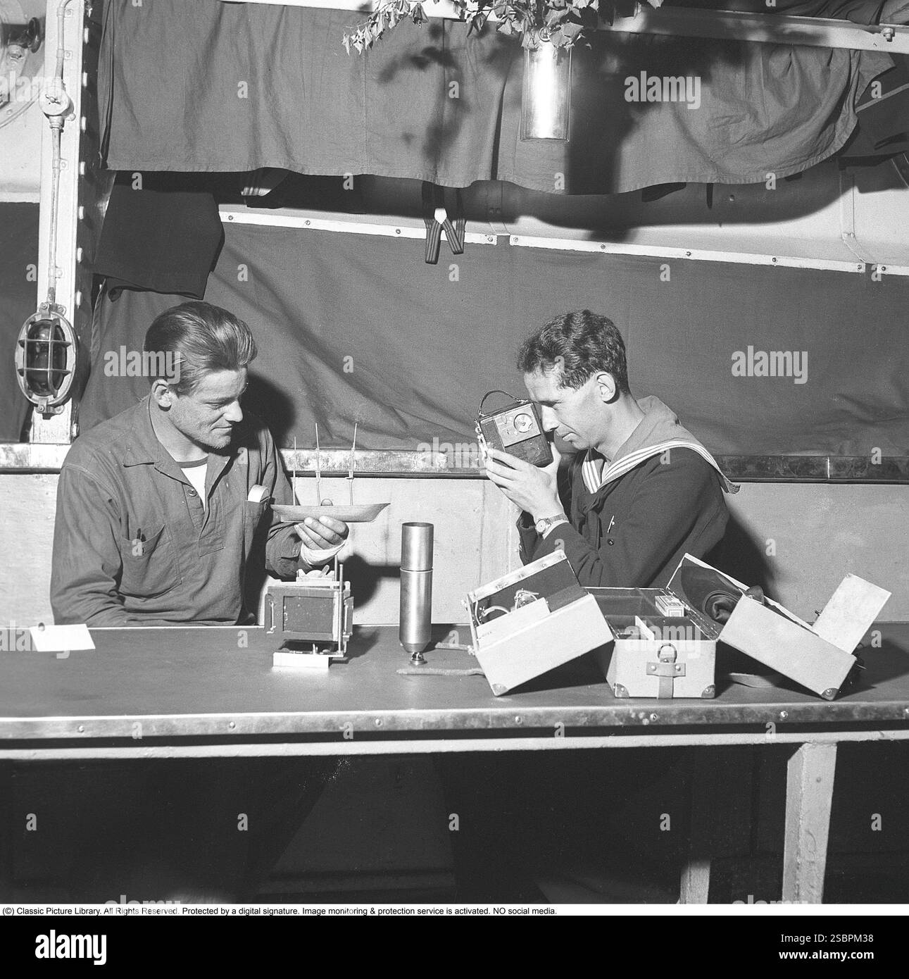 Marinai svedesi nella marina svedese nel 1942. Uno dei marinai sta reggendo un modello di una nave a vela che sembra appena iniziata, mentre l'altro sta filmando con una videocamera. Sono seduti in una delle stanze della nave dove l'equipaggio può fare altre cose quando non è in servizio. Kristoffersson rif. A63-3 Foto Stock