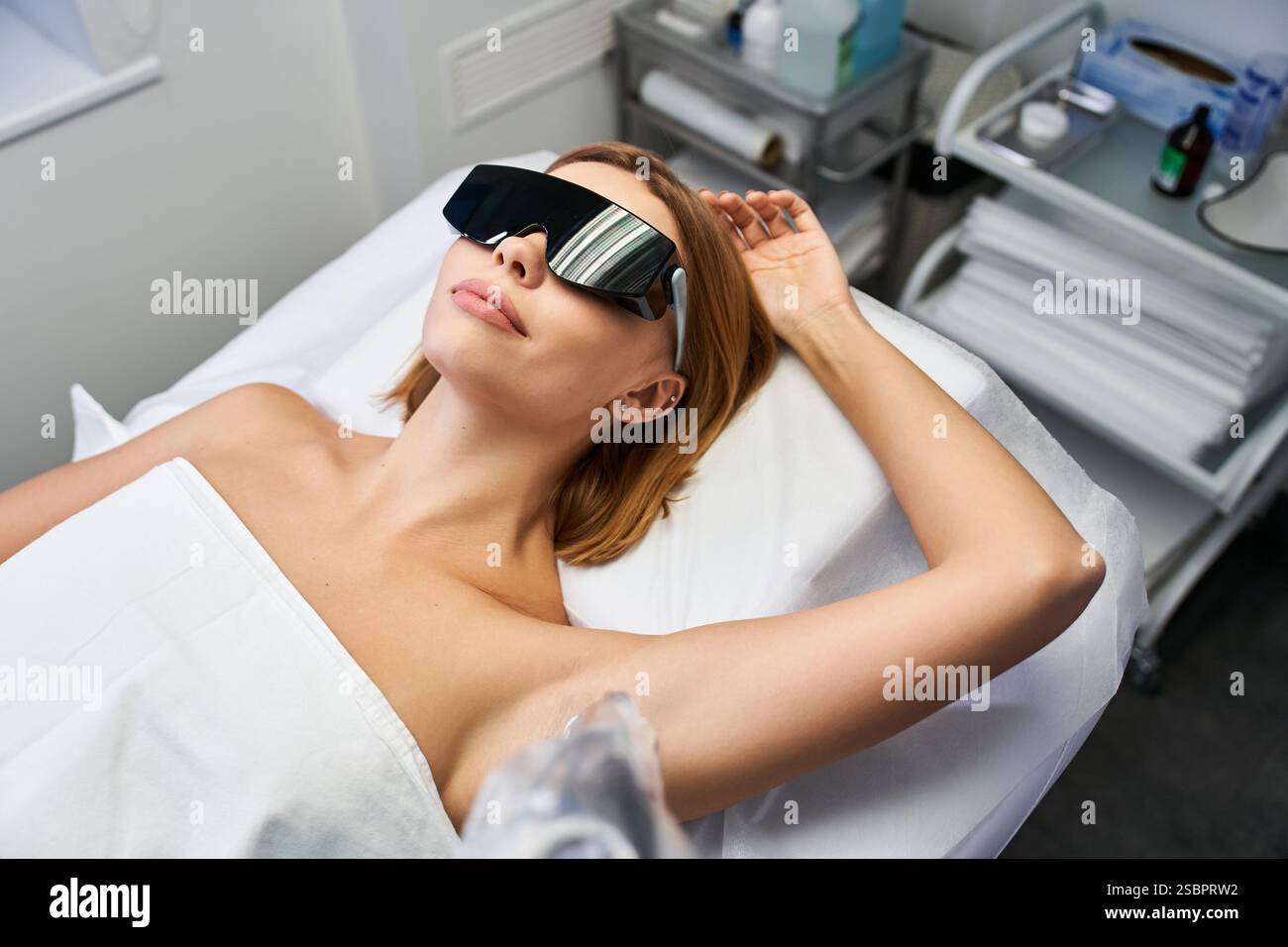 Una giovane donna si rilassa mentre riceve un trattamento di epilazione laser in un elegante ambiente clinico. Foto Stock