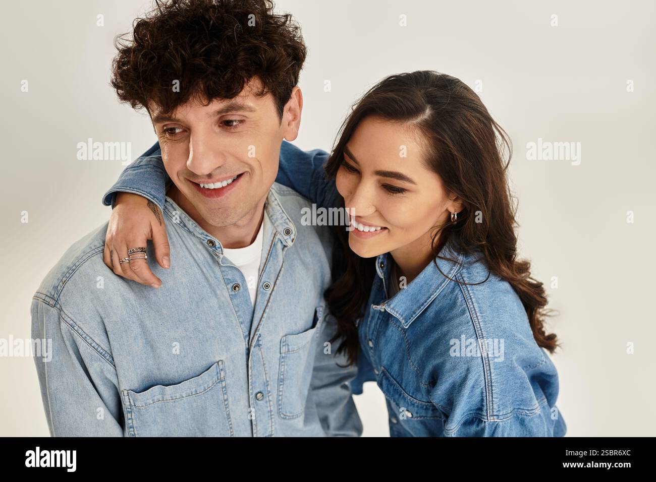 La giovane coppia sorride calorosamente mentre abbraccia, sfoggiando la moda in denim e lo stile disinvolto Foto Stock