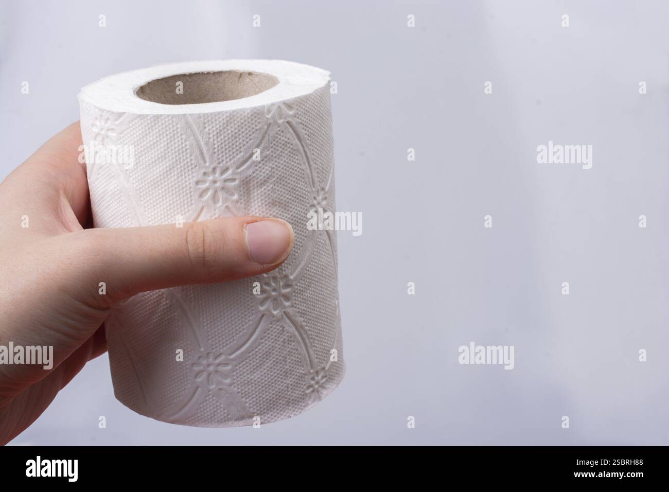Una mano femminile prende in mano un rotolo di carta igienica bianca Foto Stock