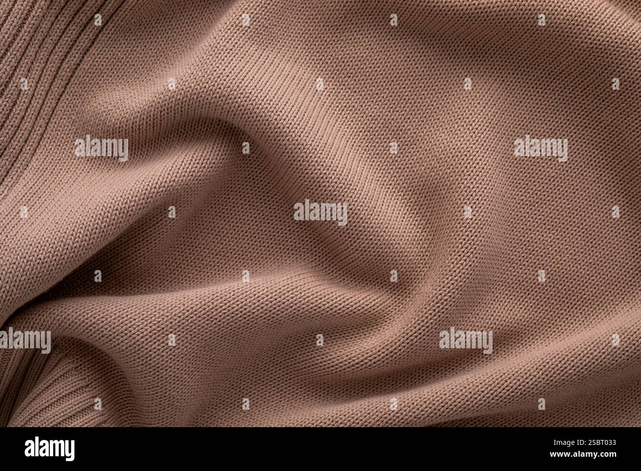 Una vista ravvicinata del morbido tessuto marrone lavorato a maglia si presenta uniformemente su una superficie piana, sottolineandone la consistenza e le pieghe delicate. La luce naturale migliora il calore e l'appeal del materiale. Foto Stock