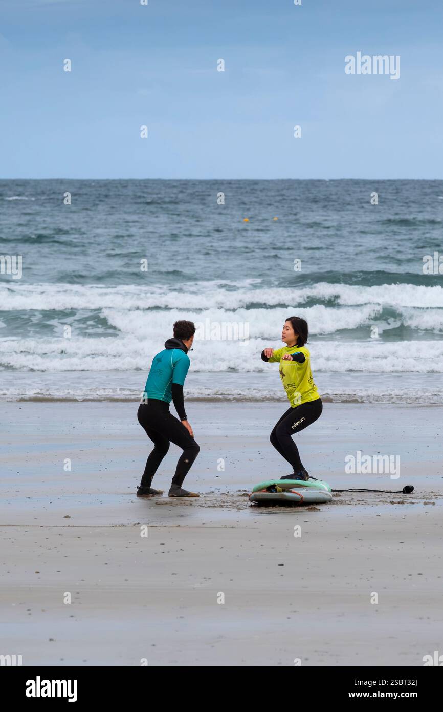 Un istruttore di surf della Escape Surfing School che tiene una lezione di surf individuale con una studentessa a Towan Beach a Newquay in Cornovaglia nel Regno Unito. Foto Stock