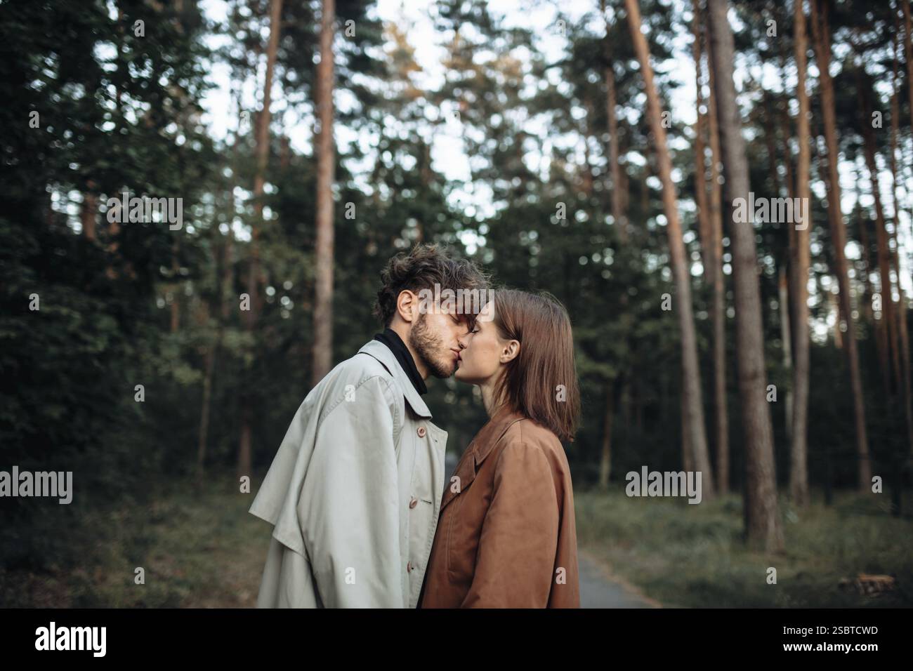 Un momento romantico con una coppia che si bacierà su un sentiero nella foresta in autunno Foto Stock