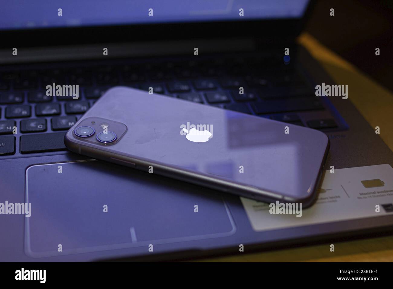 Un iPhone posizionato con il lato di stampa rivolto verso il basso sulla tastiera di un laptop, con il logo Apple Foto Stock