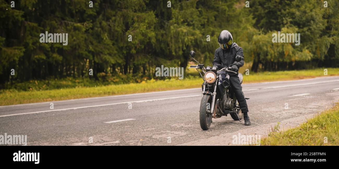 Un motociclista che indossa un casco su una strada adiacente a una foresta Foto Stock Un motociclista che indossa un casco su una strada adiacente a una foresta Foto Stock