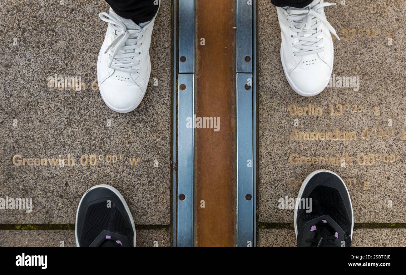 Ripresa ad alto angolo di due persone in piedi tra il Greenwich prime Meridian segnata dalla striscia di ottone sul terreno nel cortile del Royal... Foto Stock