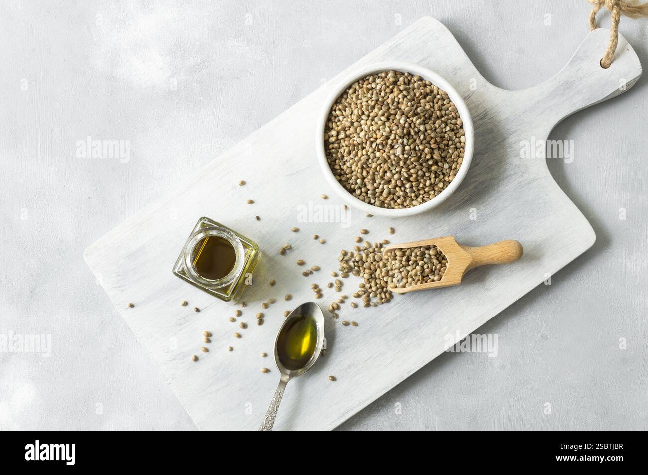 Olio di semi di canapa con un mucchio di semi di canapa organici essiccati o semi di piante di cannabis in cucchiaio o ciotola su fondo rustico, concetto di olio di erbe di cannabis Foto Stock