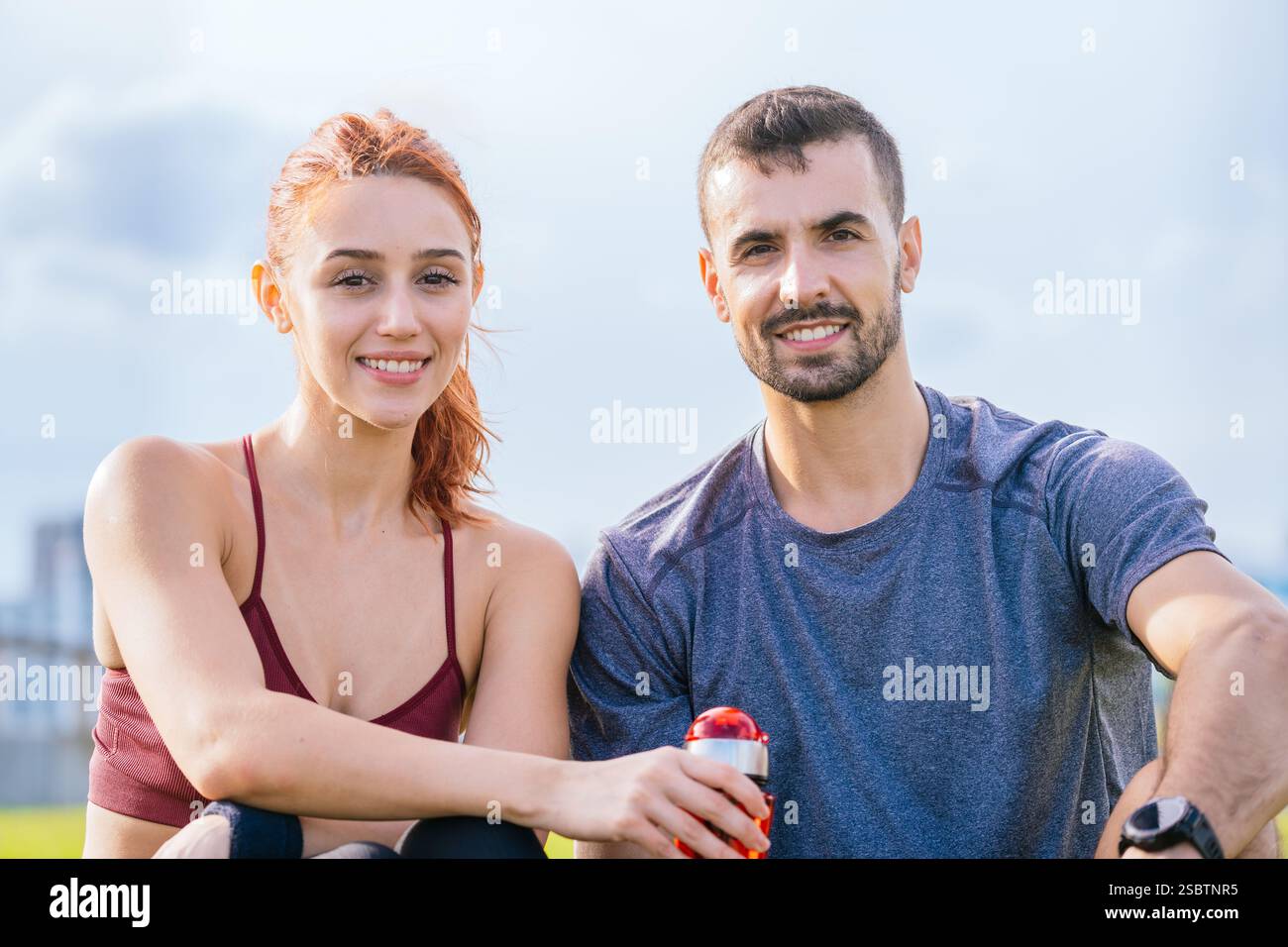 Coppia in forma sorridente che riposa all'aperto dopo l'allenamento con una bevanda rinfrescante Foto Stock